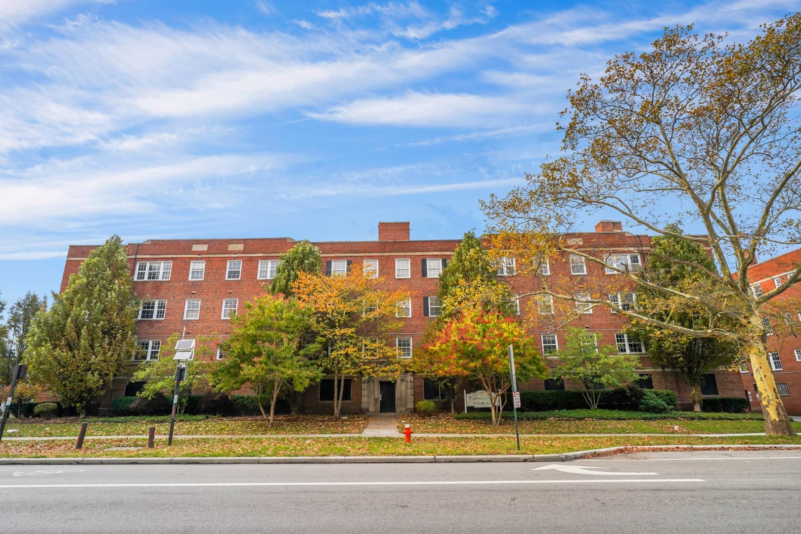 Long brick apartment facade shaded by mature street trees